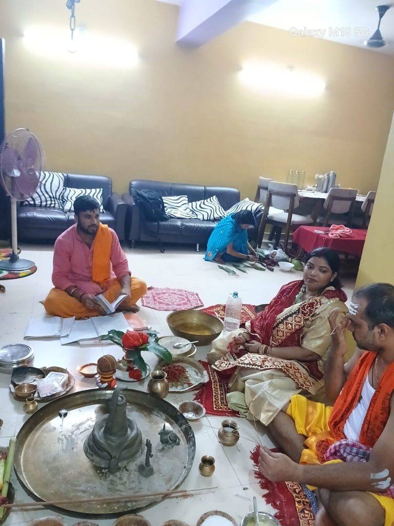 Panditji leading a significant Hindu ritual Griha Pravesh ceremony. with a couple (bride and groom) in a large room.